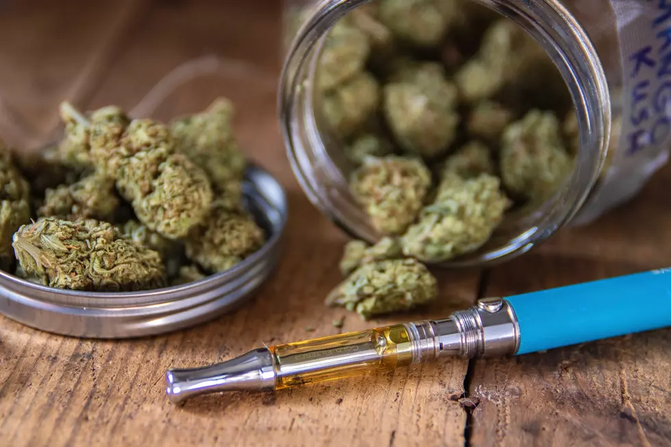Trimmed marijuana flower (Mango Kush) in glass jar on wood table with vape pen.